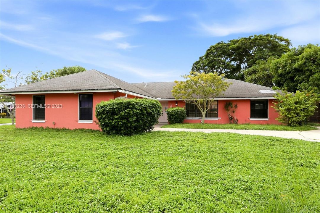 Single-story ranch-style residence featuring a stucco exterior, multi-hipped shingle roof, and expansive front yard