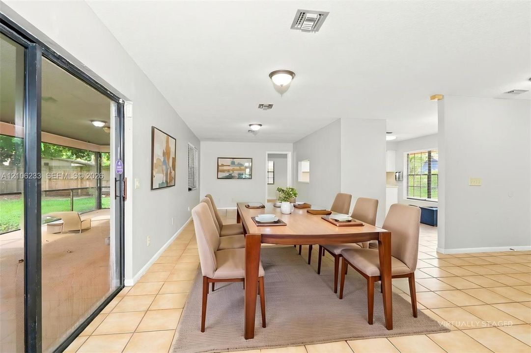 Spacious dining area featuring neutral tile flooring, recessed lighting, and a large sliding glass door providing access to a screened-in patio