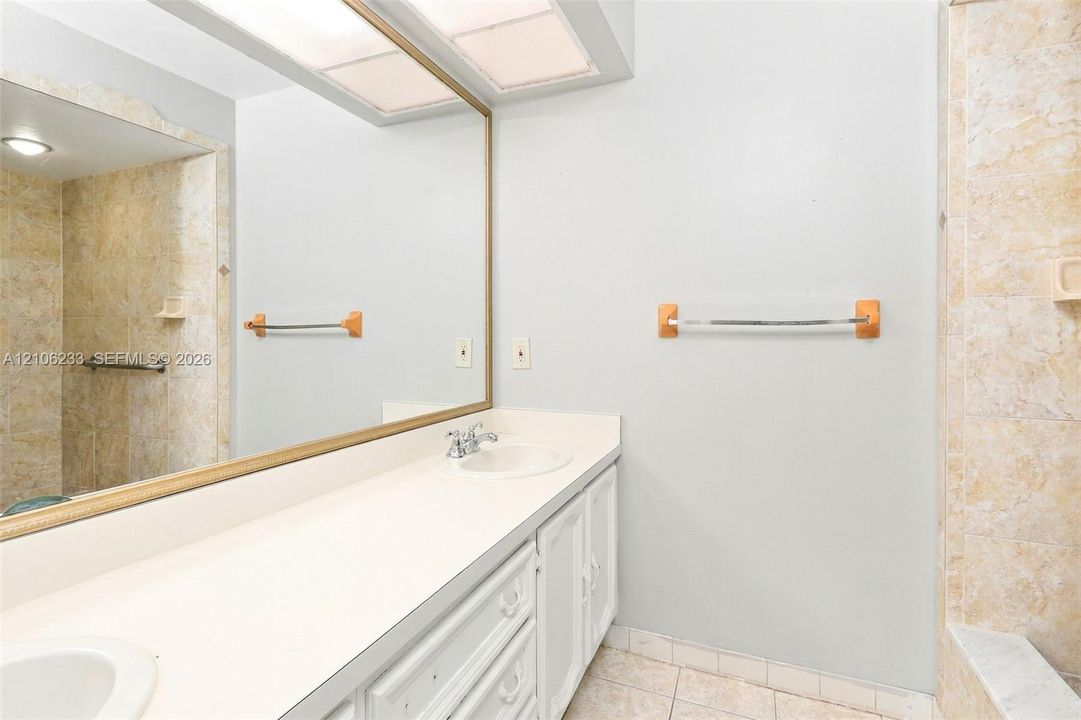 Bathroom vanity featuring a solid surface countertop, dual integrated sinks, and a large framed mirror with built-in overhead recessed lighting