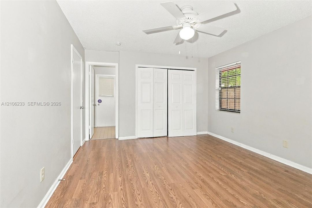 Wood-finish flooring, white bifold closet doors, neutral wall paint, and a ceiling fan with integrated lighting