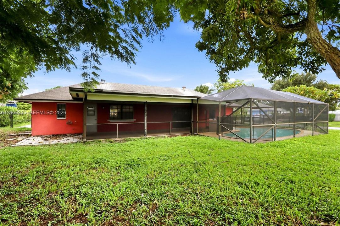 Rear exterior featuring a covered patio, screen-enclosed pool, stucco siding, and mature trees