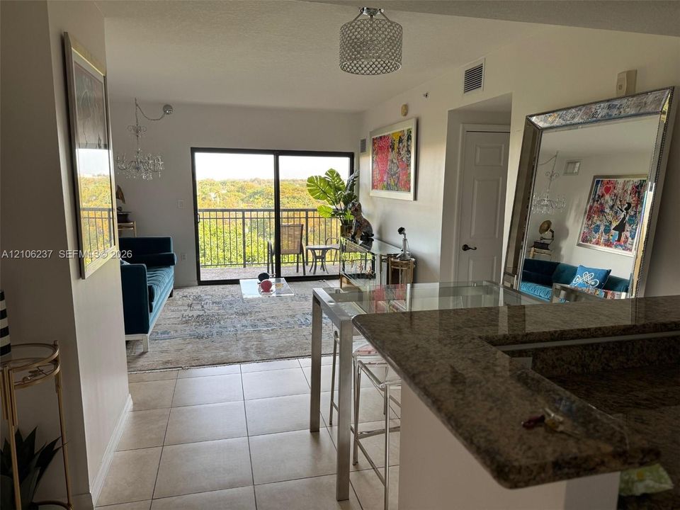 Open-concept floor plan featuring a stone-surface breakfast bar, ceramic tile flooring, a drum-style pendant light fixture, and large sliding glass doors opening to a private balcony