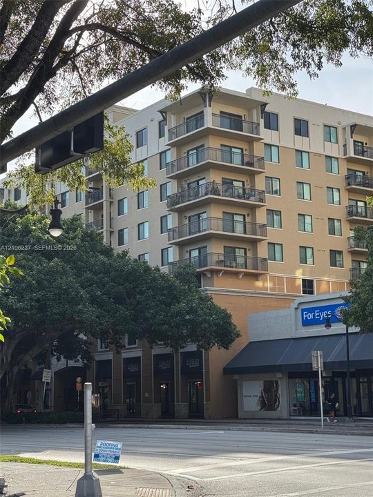 Multi-story residential building featuring private wrap-around balconies, a multi-tone facade, and ground-level commercial storefronts
