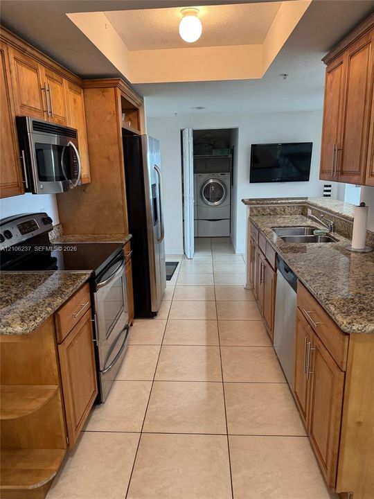 Kitchen featuring natural-finish wood cabinetry, stone countertops, stainless steel appliances, ceramic tile flooring, and an integrated laundry closet