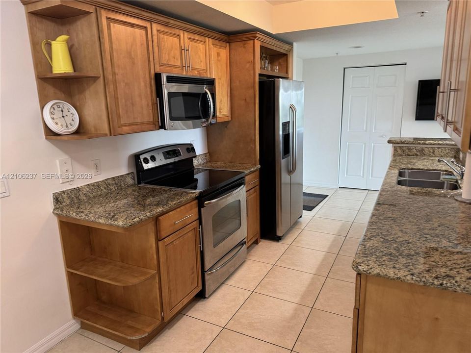 Kitchen featuring stained wood cabinetry, stone countertops, stainless steel appliances, and ceramic tile flooring