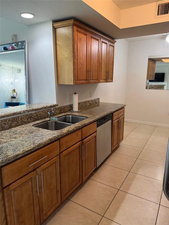 Kitchen featuring warm-tone wood cabinetry, stone-surface countertops, stainless steel dual-basin sink, integrated dishwasher, and tile flooring