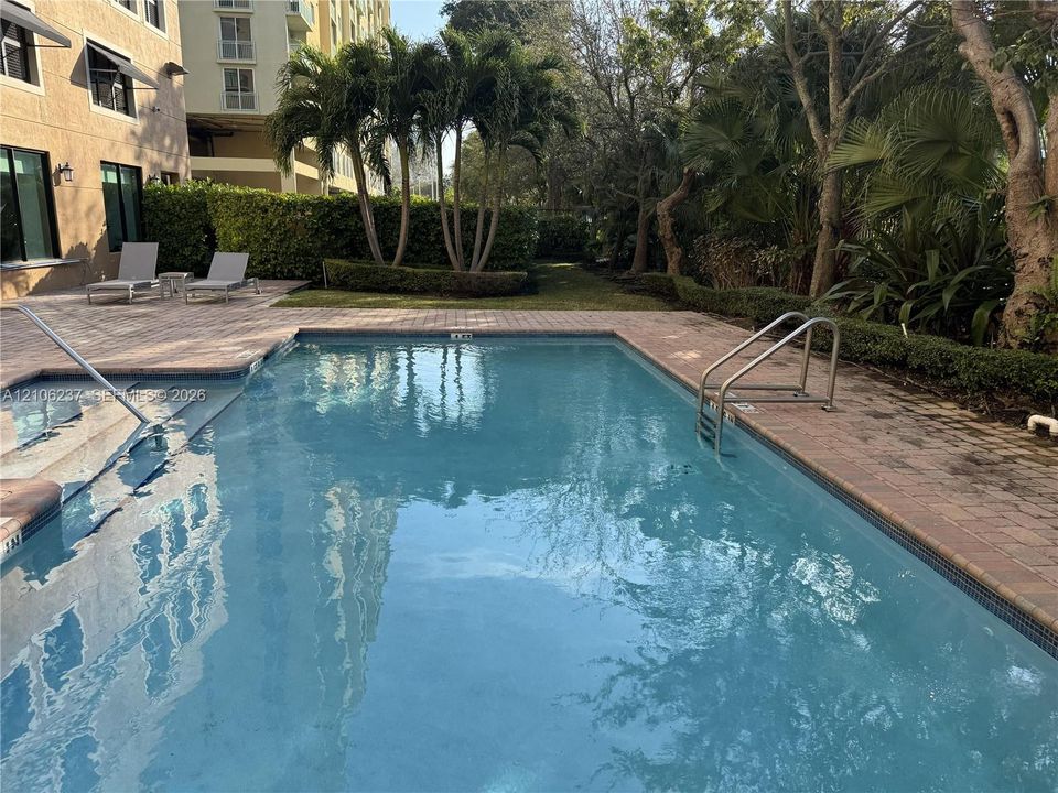 Swimming pool featuring paver decking, metal handrails, integrated steps, and mature landscaping