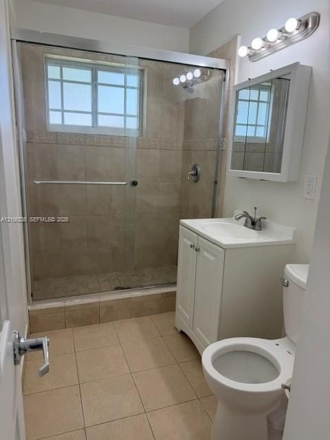 Bathroom featuring a glass-enclosed shower with tile surround, neutral-toned floor tiling, white vanity cabinet with a ceramic sink, and a wall-mounted mirrored medicine cabinet