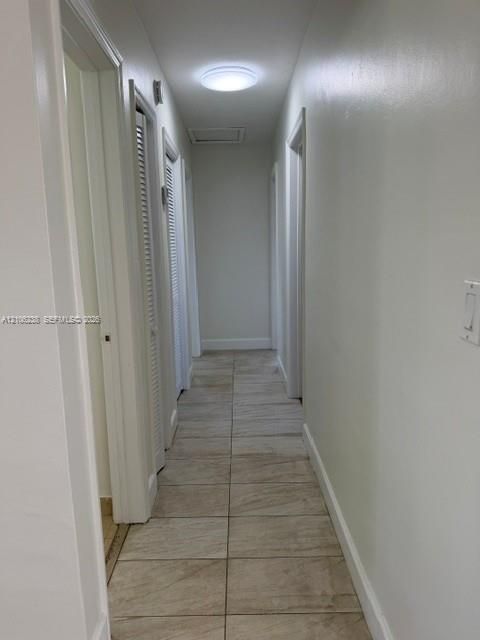 Hallway featuring neutral-toned tile flooring, flush-mount lighting, and dual louvered-style closet doors