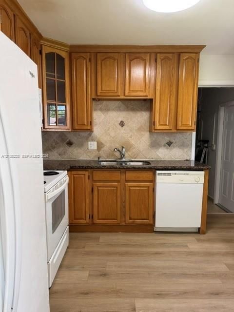 Kitchen featuring wood cabinetry, stone-finish countertops, tile backsplash, stainless steel dual-basin sink with a gooseneck faucet, and wood-finish flooring