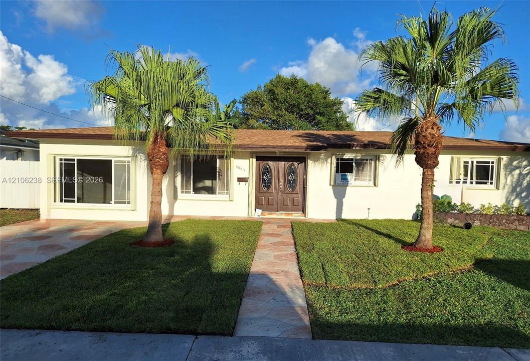 Single-story exterior featuring a light-toned stucco façade, double entry doors with decorative glass inserts, palm tree landscaping, and a flagstone walkway