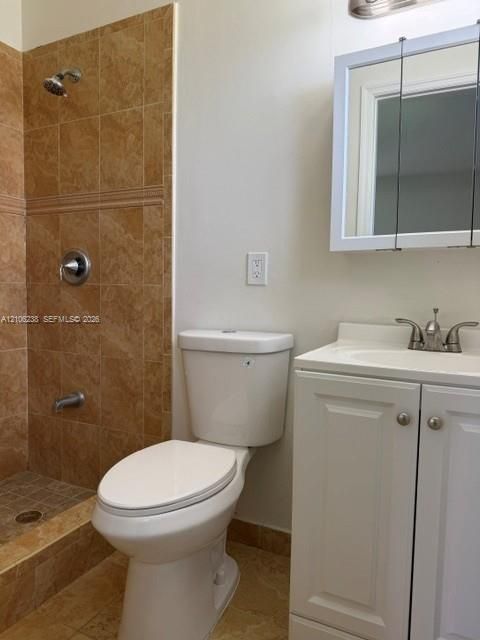 Shower stall featuring full-height stone-finish tile surround and a built-in stone ledge, white vanity cabinet with a integrated sink, and medicine cabinet with mirrored doors