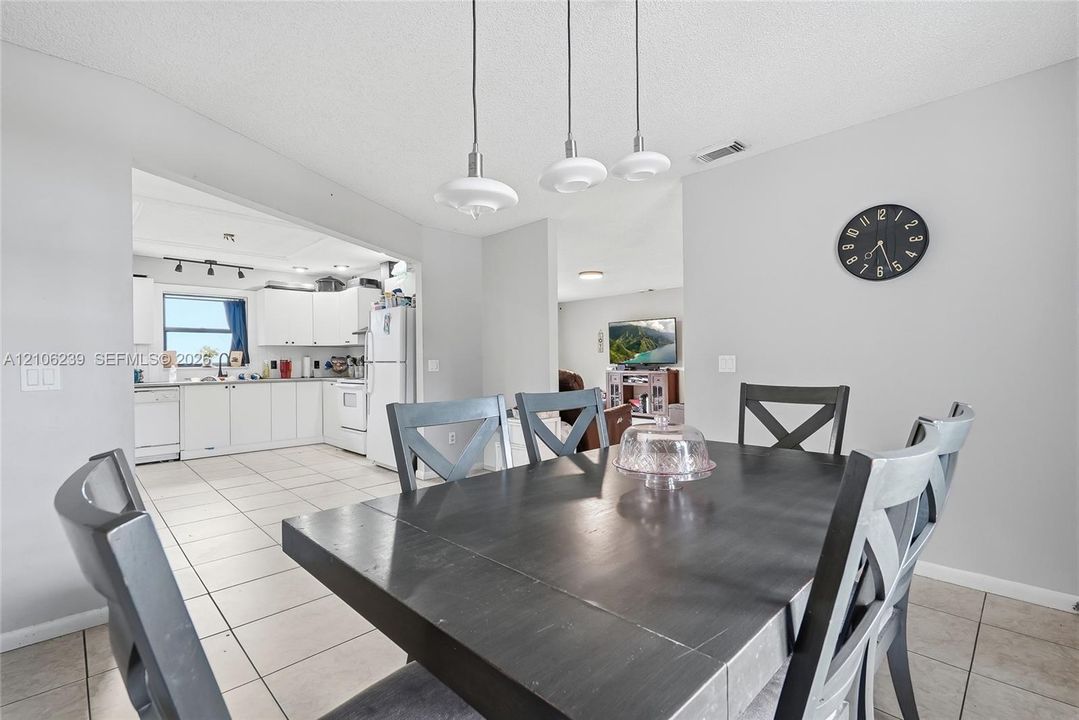 Dining area featuring neutral tile flooring and three pendant light fixtures, showcasing kitchen cabinetry, white appliances, and a window