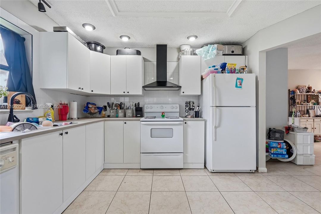 Kitchen featuring white cabinetry, solid-surface countertops, tile flooring, and a black range hood