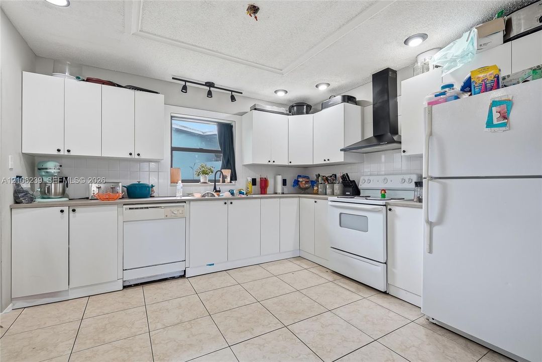 Kitchen featuring white cabinetry, ceramic tile flooring, a black wall-mounted range hood, and recessed lighting