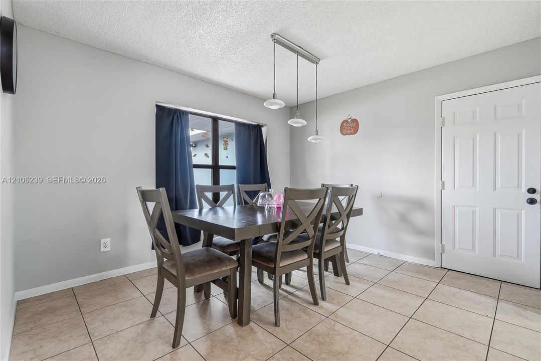 Neutral-tone interior featuring large-format ceramic tile flooring, a multi-pendant linear light fixture, and a six-panel exterior door