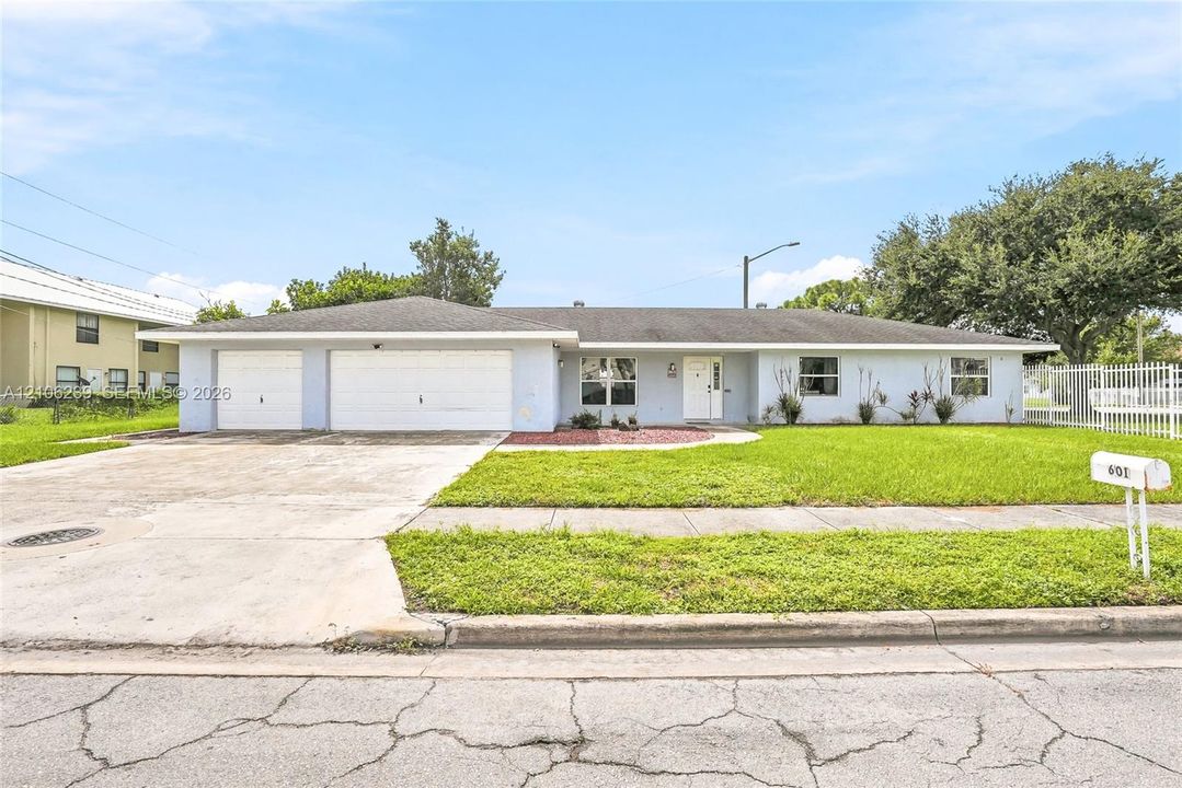 Single-story exterior featuring a low-slope roof, two-car garage, concrete driveway, and white metal fencing