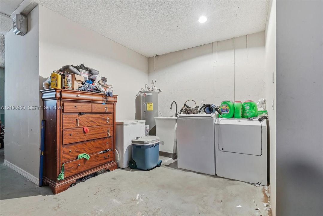 Utility area featuring a deep basin sink with a high-arch faucet, dedicated water heater, and concrete flooring