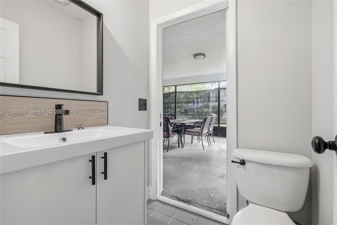 White vanity featuring black hardware, a rectangular basin, and a wood-finish backsplash, complemented by a black-framed mirror, matte black faucet, and a standard-height toilet