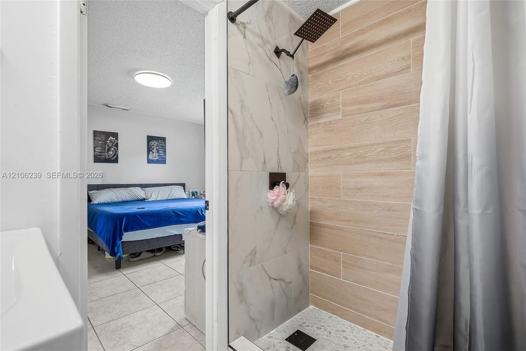 Shower featuring large-format stone-patterned tile, wood-finish wall tile, and a rectangular rainfall showerhead in a matte black finish