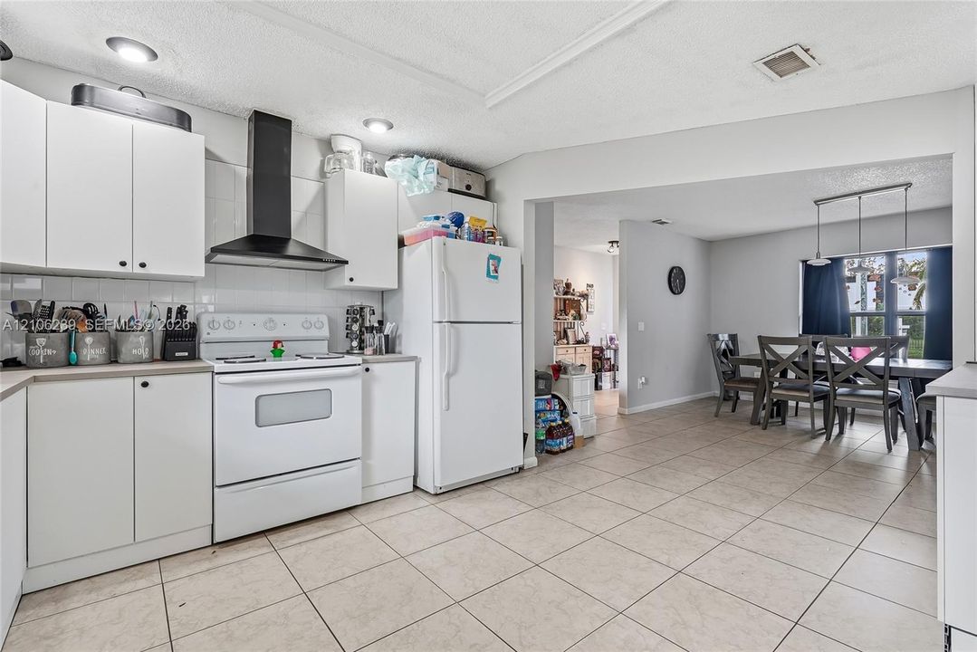 Kitchen featuring white cabinetry, contrasting black range hood, white appliances, and ceramic tile flooring