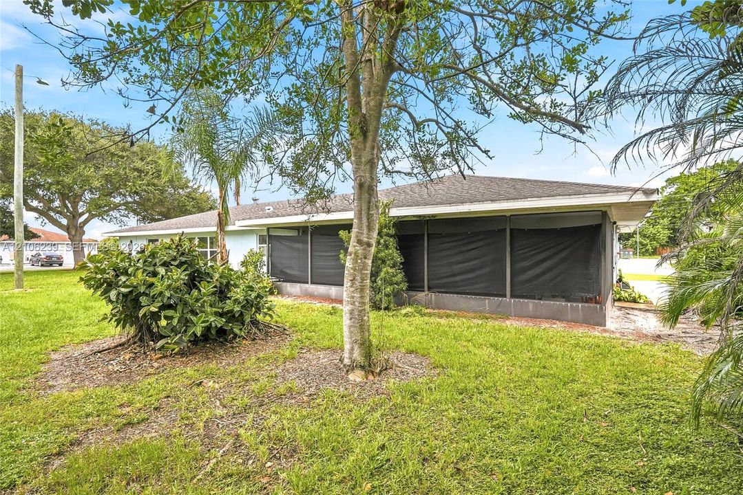 Exterior featuring a screened-in lanai, hip roofline, and expansive lawn with mature trees