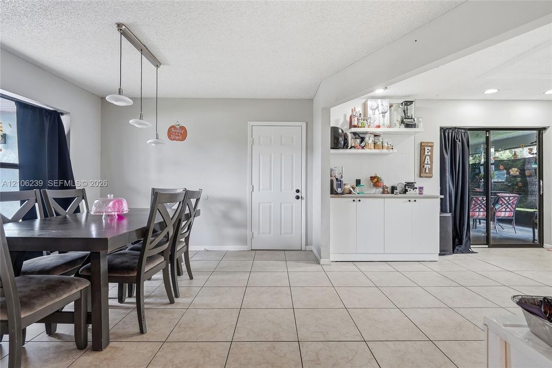Ceramic tile flooring, built-in lower cabinetry with a solid surface countertop, open shelving, three-light linear pendant fixture, and sliding glass door