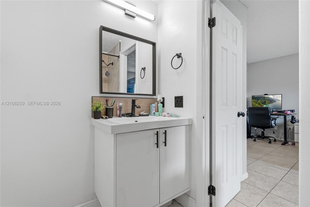 Bathroom vanity featuring a rectangular integrated sink, matte black faucet, dark-framed mirror, and minimalist cabinetry hardware, illuminated by a linear LED wall light fixture