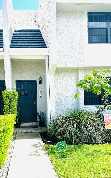Stucco exterior with a paneled front entry door, dark-toned shingle accents, and a concrete walkway