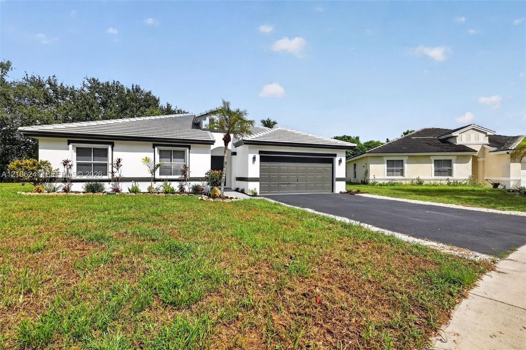 Single-story exterior featuring light-toned stucco, contrasting dark trim, a tiled roof, an attached two-car garage, and an asphalt driveway
