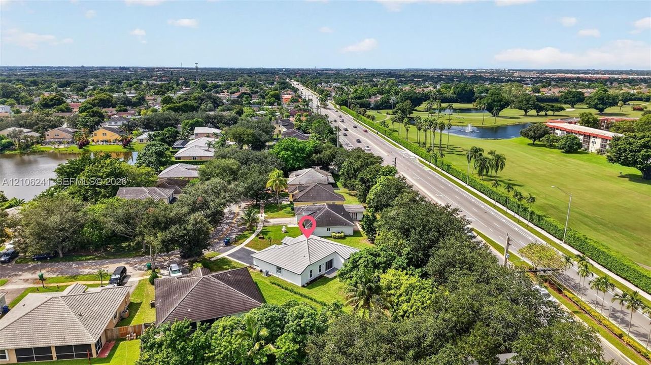 Aerial perspective of a single-story residence featuring a hipped roofline, paved driveway, expansive lawn, and mature canopy trees