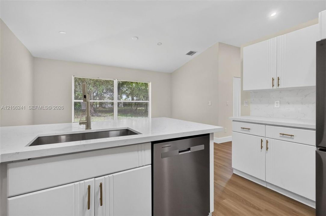 Kitchen featuring white shaker-style cabinetry, stone-surface countertops, recessed lighting, wood-finish flooring, and a stainless steel undermount sink with a high-arch faucet