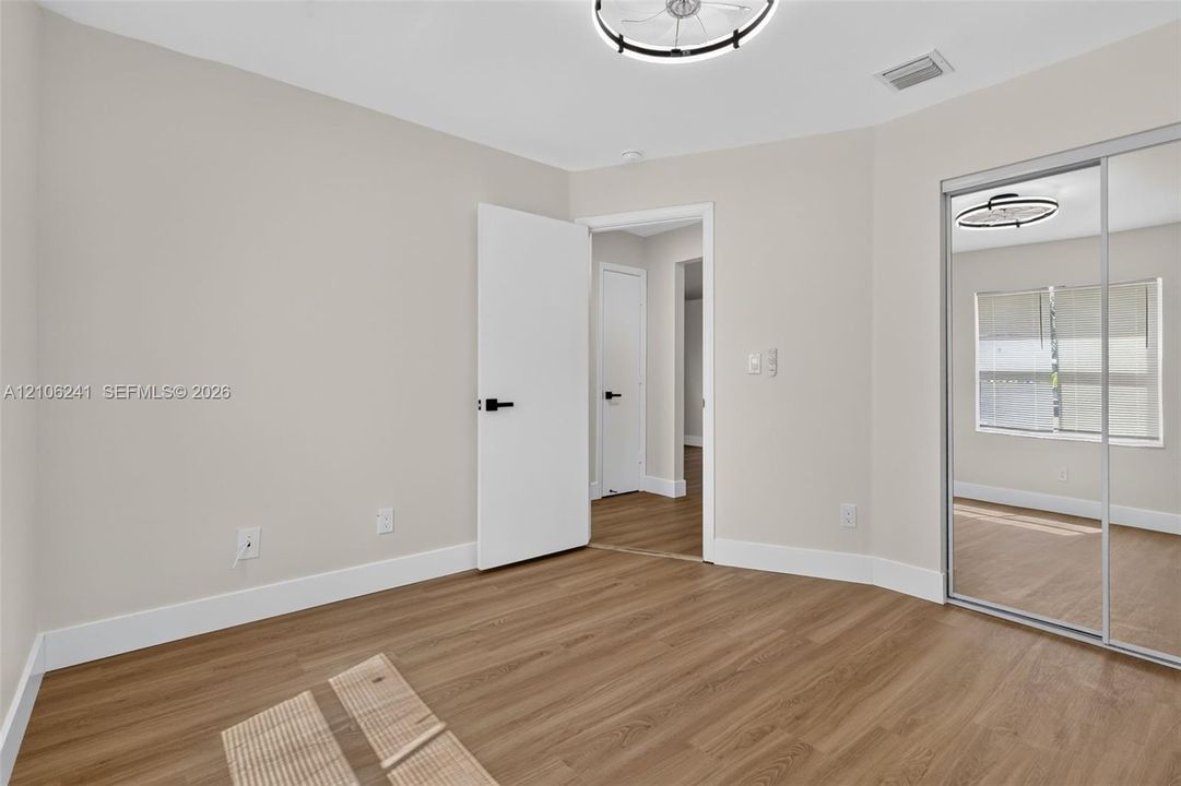 Neutral-toned interior featuring wood-finish flooring, sliding mirror-panel closet doors, and modern circular flush-mount lighting with matte black hardware