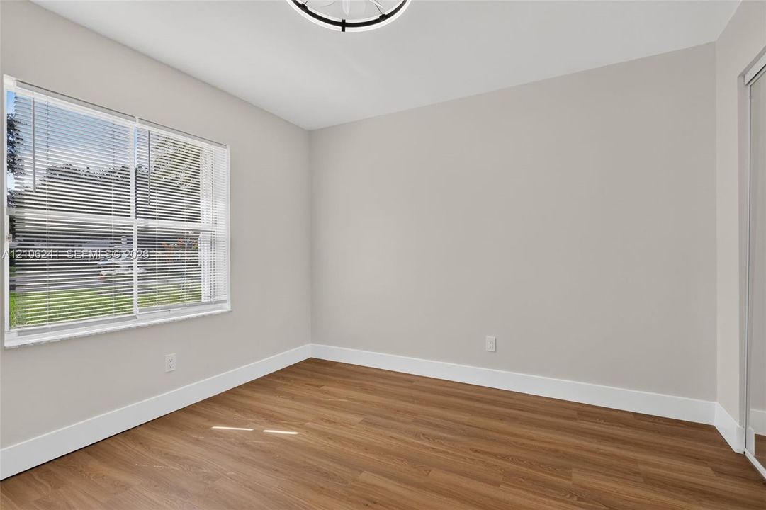 Neutral interior featuring wood-finish flooring, a multi-pane window with horizontal blinds, a contemporary drum-style ceiling light fixture, and mirrored closet doors