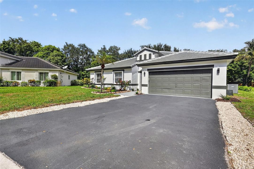 Single-story exterior featuring a multi-gabled roofline, light-toned stucco facade, multi-panel garage door, and a paved driveway lined with stone accents