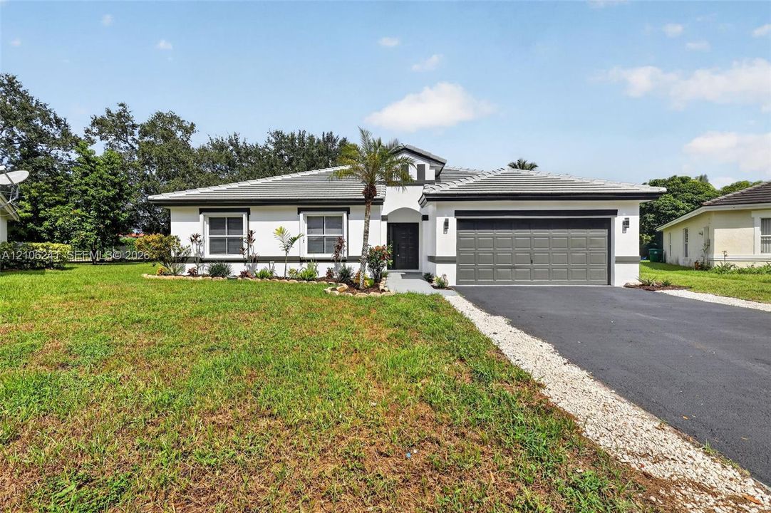 Single-story exterior featuring white stucco siding, a grey tile roof, a two-car garage, and a paved driveway