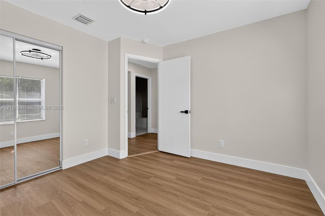 Neutral interior featuring wood-finish flooring, sliding mirror-panel closet doors, and matte black hardware