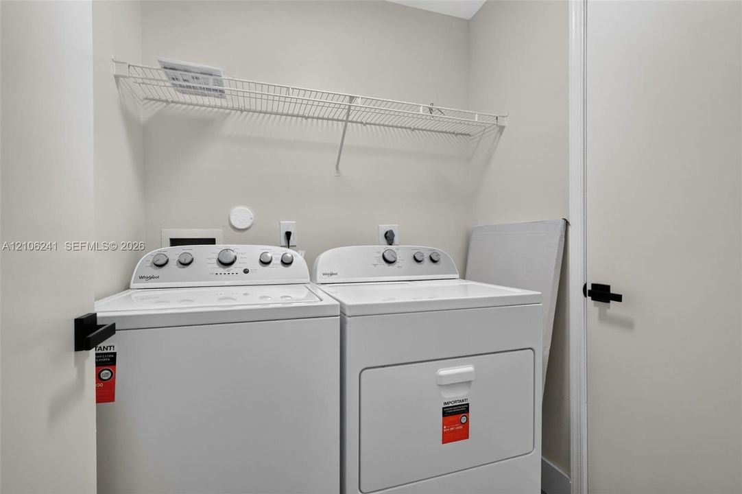 Laundry area featuring white top-load washer and dryer, mounted wire shelving, and matte black door hardware