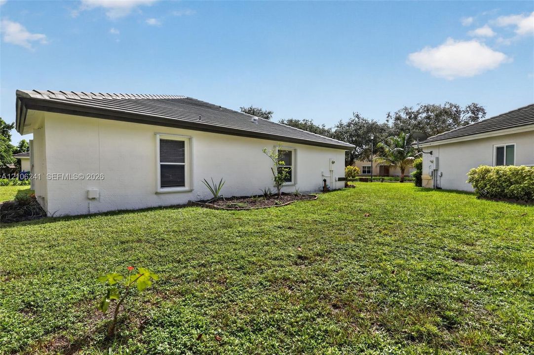 Exterior elevation featuring light-colored stucco siding, a low-pitch roof, inset single-hung windows, and a grass-covered backyard