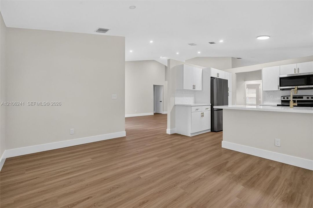 Interior featuring wood-finish flooring, vaulted ceilings, recessed lighting, white cabinetry, and a peninsula with a stone-surface countertop