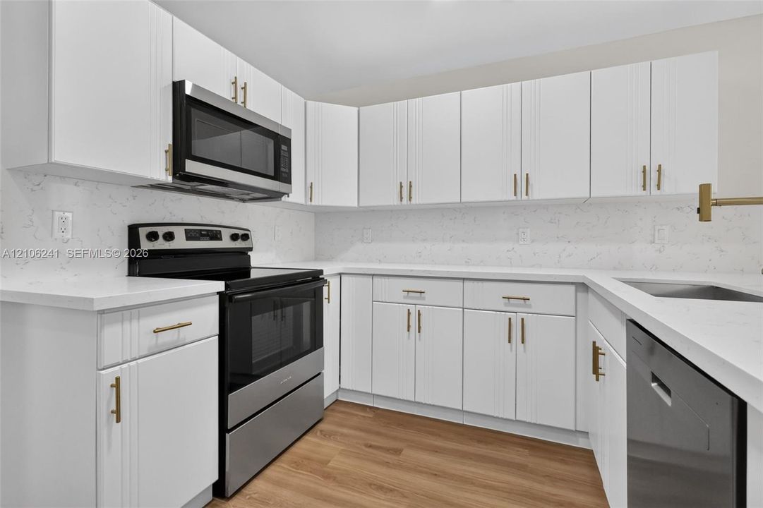 Kitchen featuring white shaker-style cabinetry, quartz countertops, full-height stone-patterned backsplash, stainless steel appliances, and wood-finish flooring
