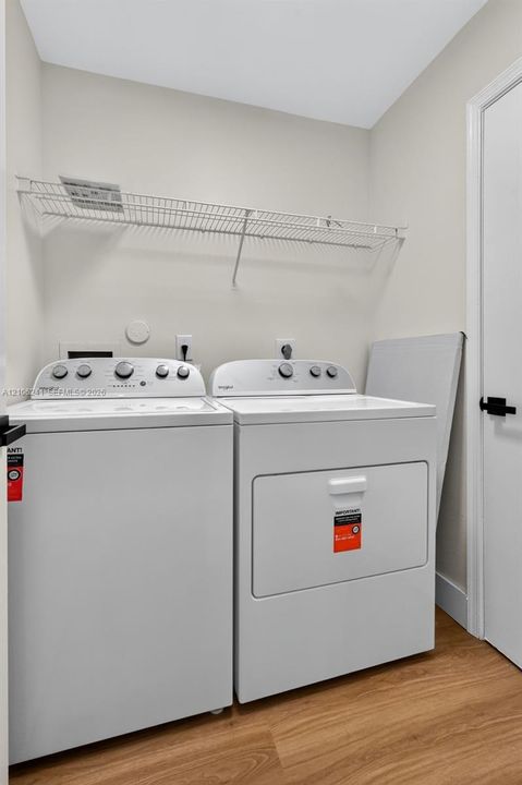 Laundry area featuring wood-finish flooring, white Whirlpool top-load appliances, and wall-mounted white wire shelving
