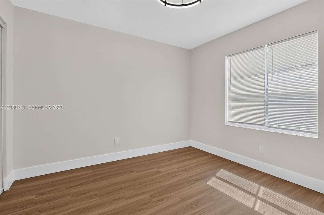 Neutral-toned walls, wood-finish flooring, a window with horizontal blinds, and a circular LED flush-mount ceiling light