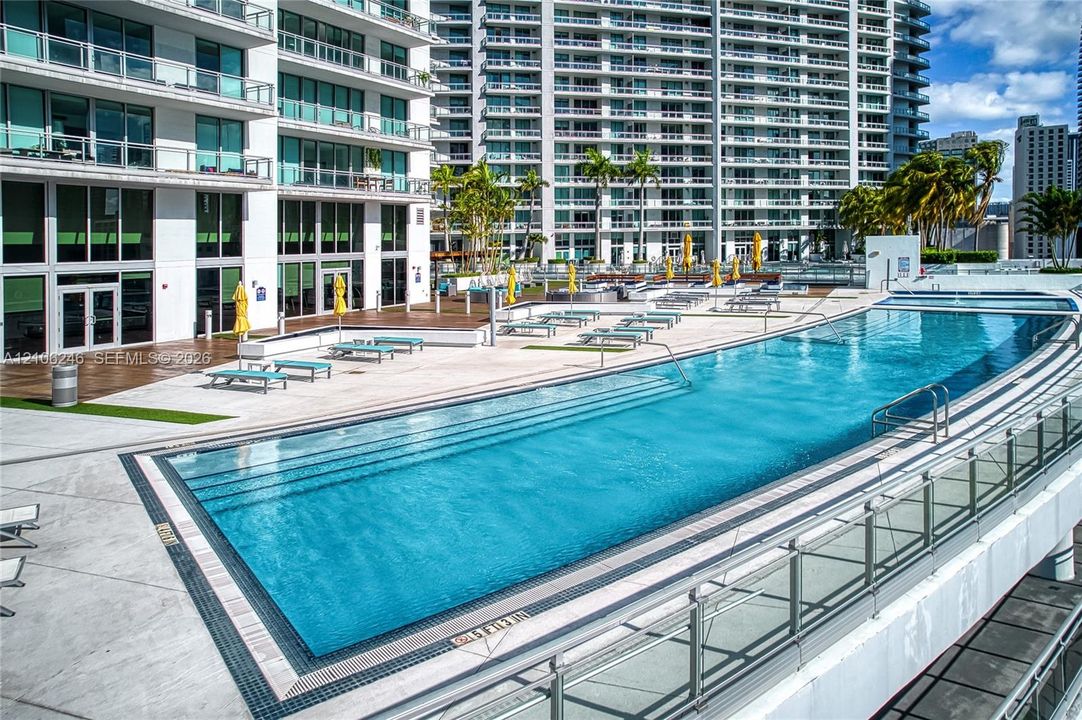 Expansive swimming pool with integrated stair entry, surrounded by a paved sun deck and wood-finish decking