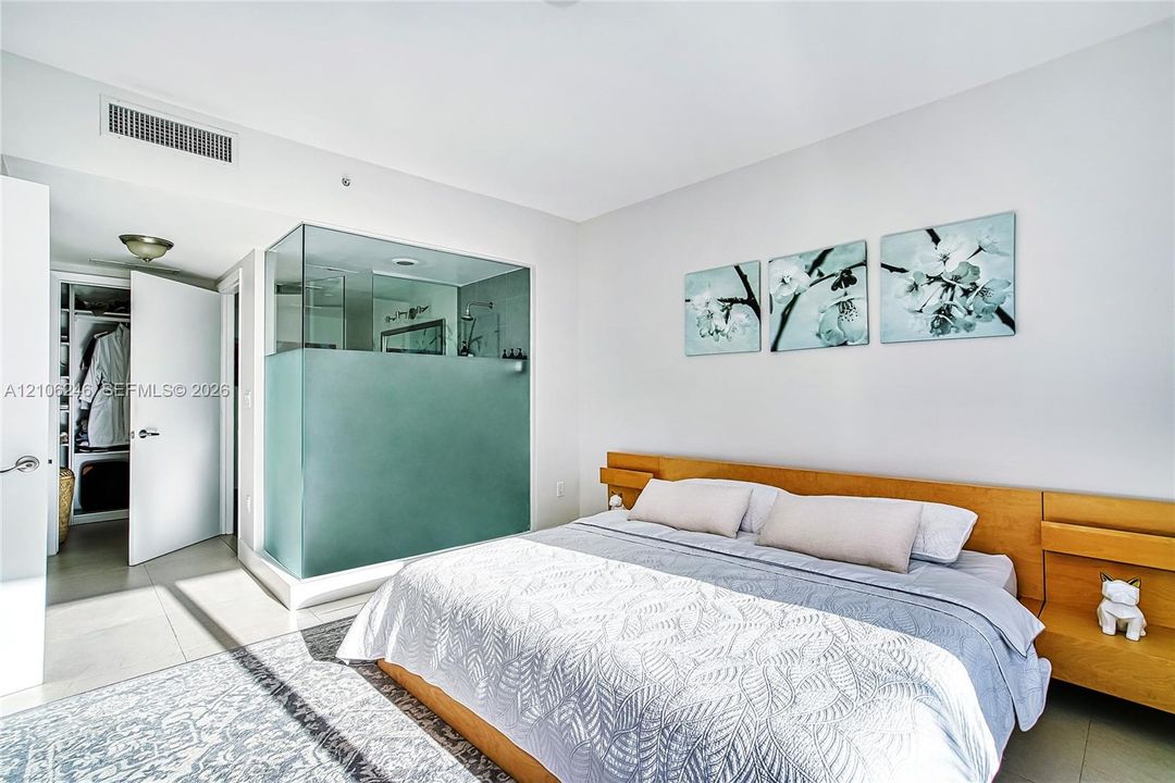 Glass-enclosed shower featuring a frosted privacy panel, built-in wooden headboard with integrated shelving, and large-format tile flooring