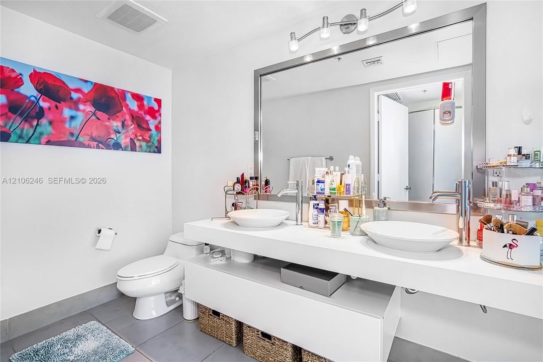 Floating vanity featuring dual vessel sinks, chrome-finish faucets, a full-width mirror with a stainless steel frame, and multi-bulb vanity lighting