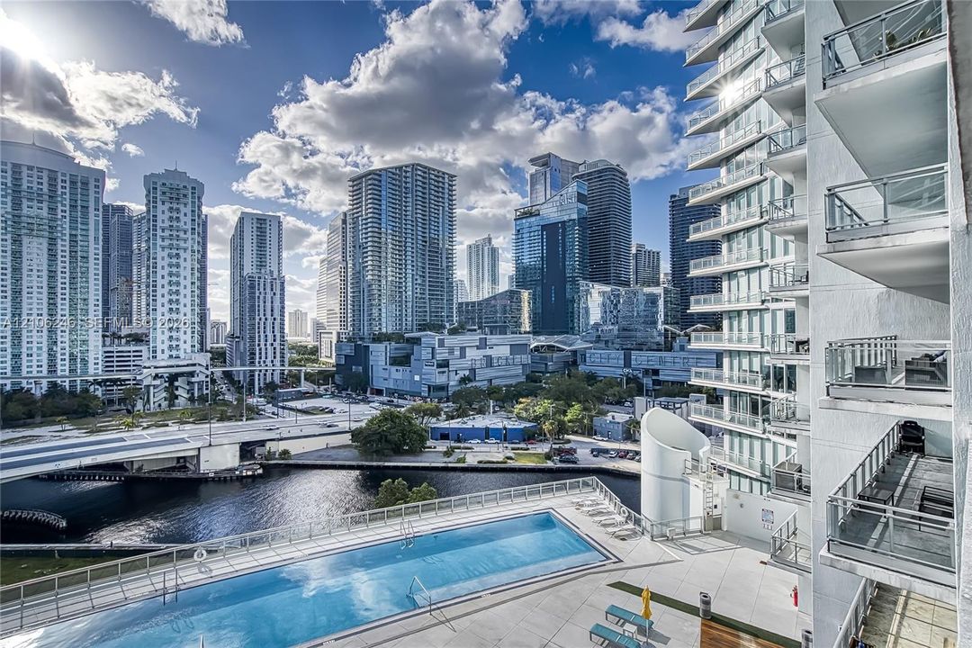 Rectangular outdoor swimming pool with a concrete pool deck, multi-level glass-paneled balconies, and architectural skyscraper exterior