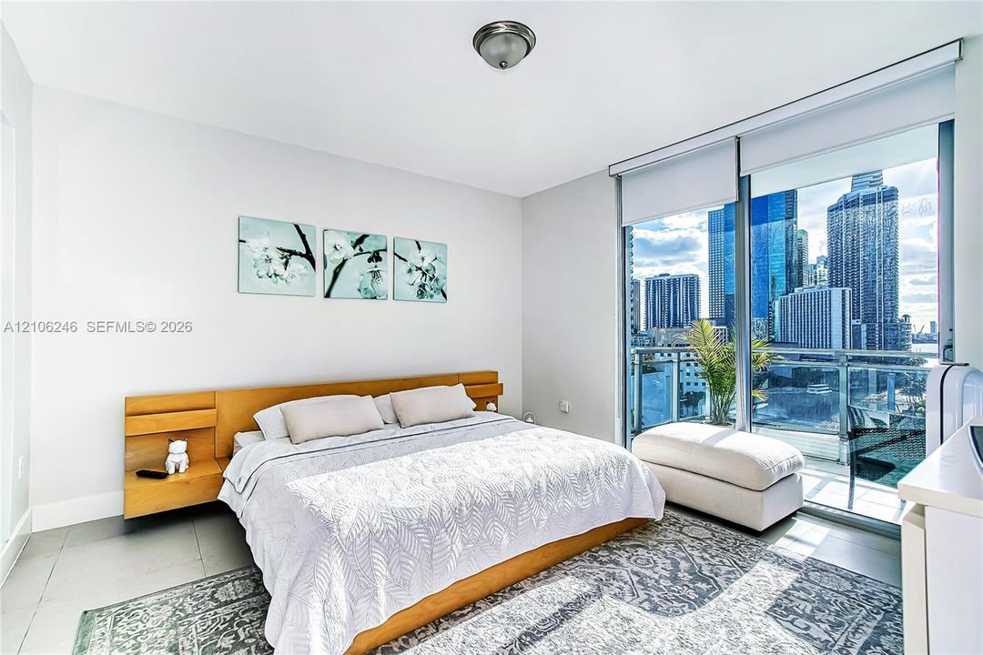 Floor-to-ceiling glass wall, private balcony with metal railing, neutral tile flooring, and integrated wood-finish headboard