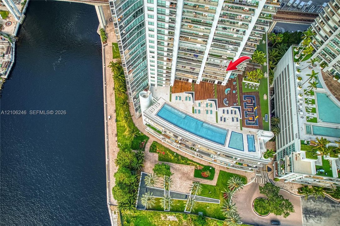 High-rise property featuring an expansive outdoor recreation deck with a multi-level swimming pool, manicured lawn areas, wood-finish decking, and direct water frontage