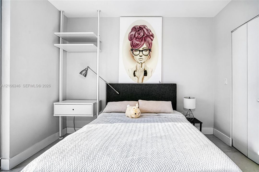 Built-in white shelving system featuring an integrated floating storage drawer and wall-mounted task lighting, complemented by a floor-to-ceiling closet with dual panel doors